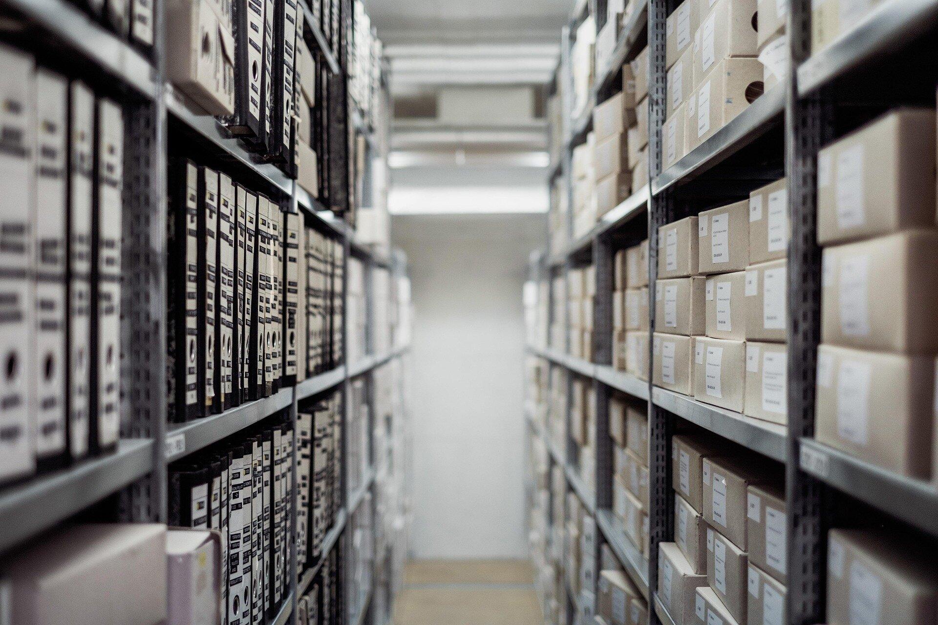 Rows of labelled archive boxes receding into soft focus — an institutional archive waiting, mostly unread.