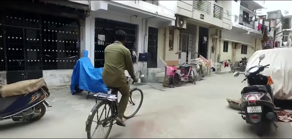 Man cycling down a narrow lane past parked scooters
